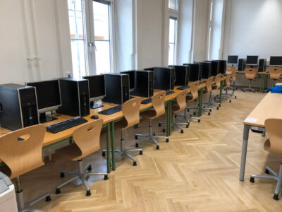 Ein IT Saal der AHS-Rahlgasse. Zu sehen sind mehrere Computer, die an einer Wand in einer Reihe stehen.